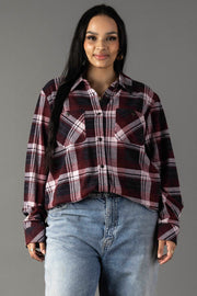 A woman with long dark hair, dressed in the Panache Apparel Collection’s Maroon, Charcoal & White Plaid Button Up and light blue jeans, stands against a plain gray background, smiling slightly at the camera.