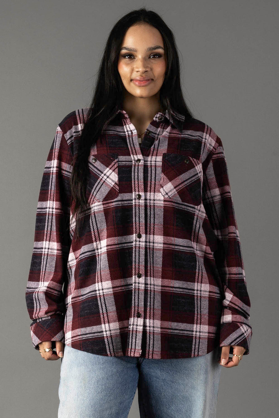 A woman with long dark hair wears the Panache Apparel Collection Maroon, Charcoal & White Plaid Button Up and light blue jeans. She stands facing the camera against a plain gray background, smiling slightly.