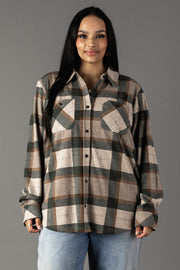 A woman with long dark hair wears the Panache Apparel Collection’s Tan, Dark Green & Rust Plaid Button Up, paired with light blue jeans as she stands against a plain gray background, smiling gently at the camera.