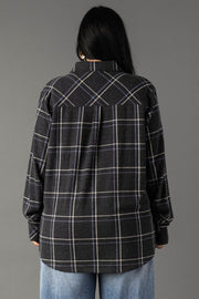 A person with long black hair wears the Panache Apparel Collection’s Dark Gray, Light Blue & White Plaid Button Up shirt and light blue jeans, standing with their back to the camera against a plain gray background.