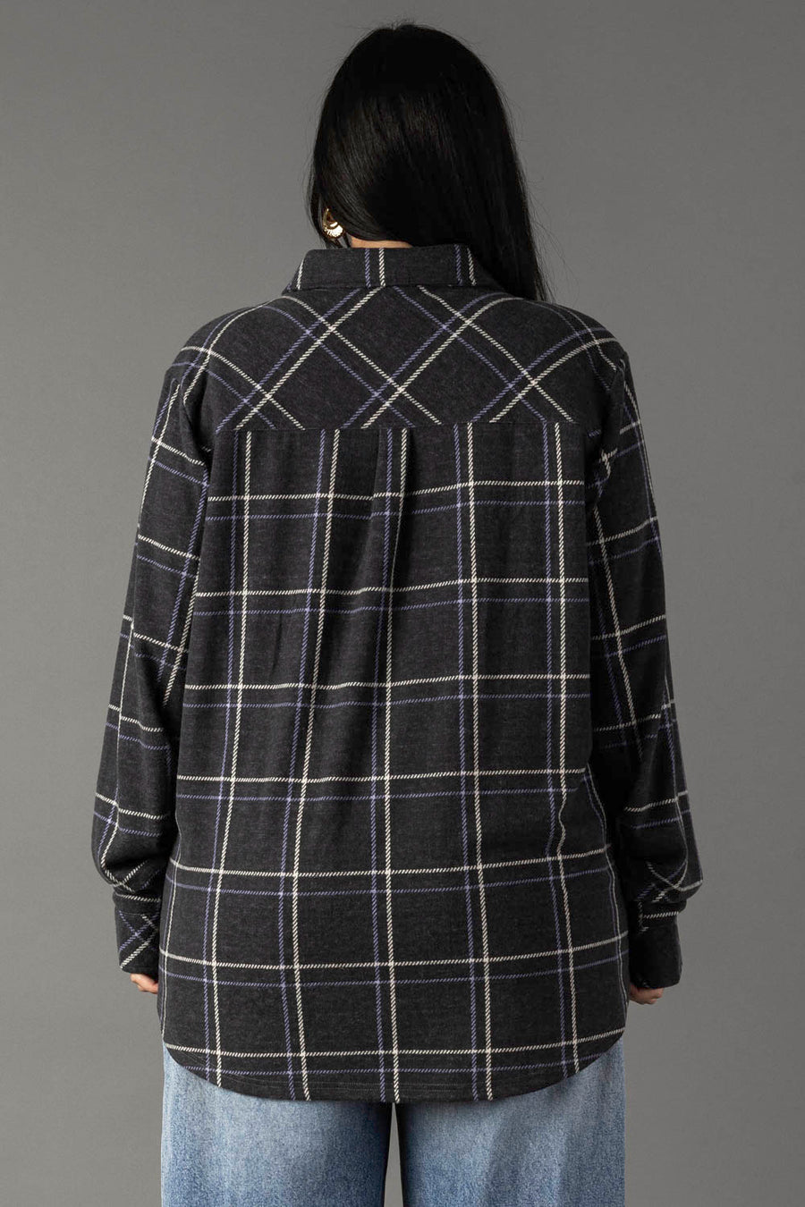 A person with long black hair wears the Panache Apparel Collection’s Dark Gray, Light Blue & White Plaid Button Up shirt and light blue jeans, standing with their back to the camera against a plain gray background.