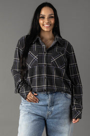 A woman with long dark hair wears the Panache Apparel Collection Dark Gray, Light Blue & White Plaid Button Up, paired with light blue jeans and smiles while standing against a plain gray background.