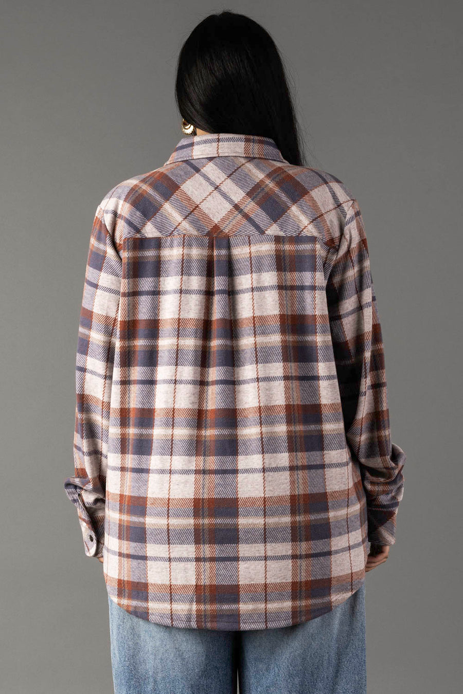 A person with long dark hair, seen from behind, is wearing the Panache Apparel Collection Dusty Blue, Brick & Tan Plaid Button Up and light blue jeans against a plain gray background.