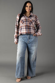 A woman smiles as she stands against a plain gray background, wearing the Panache Apparel Collection’s Dusty Blue, Brick & Tan Plaid Button Up paired with loose-fitting blue jeans.