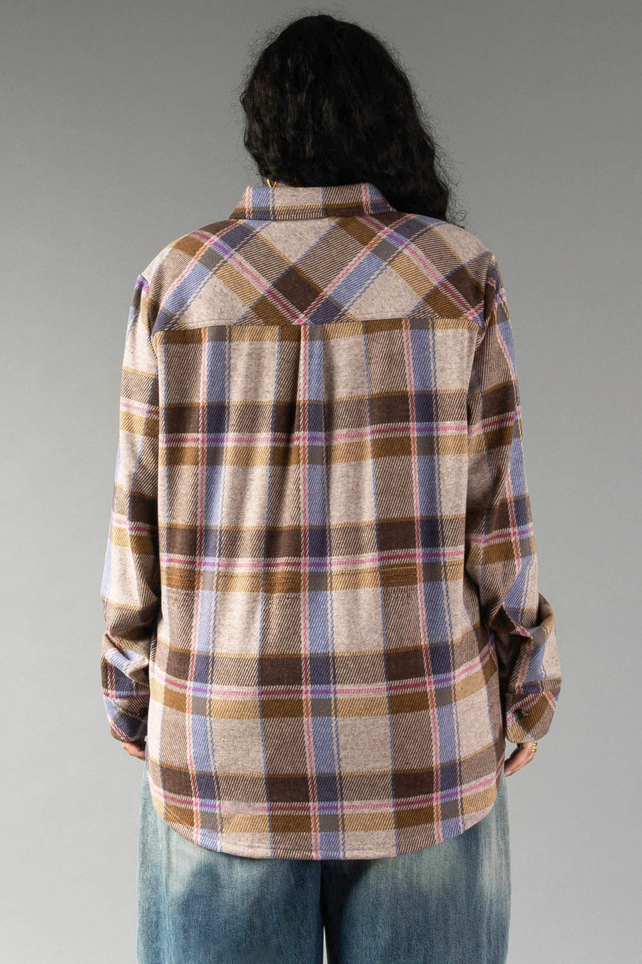 A person with long dark hair, seen from behind, wears the Panache Apparel Collection Dark Brown, Blue & Pink Plaid Button Up and blue jeans, standing against a plain gray background.