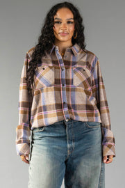 A woman with long curly hair models the Panache Apparel Collection’s Dark Brown, Blue & Pink Plaid Button Up, styled with blue jeans and posed against a plain gray background.