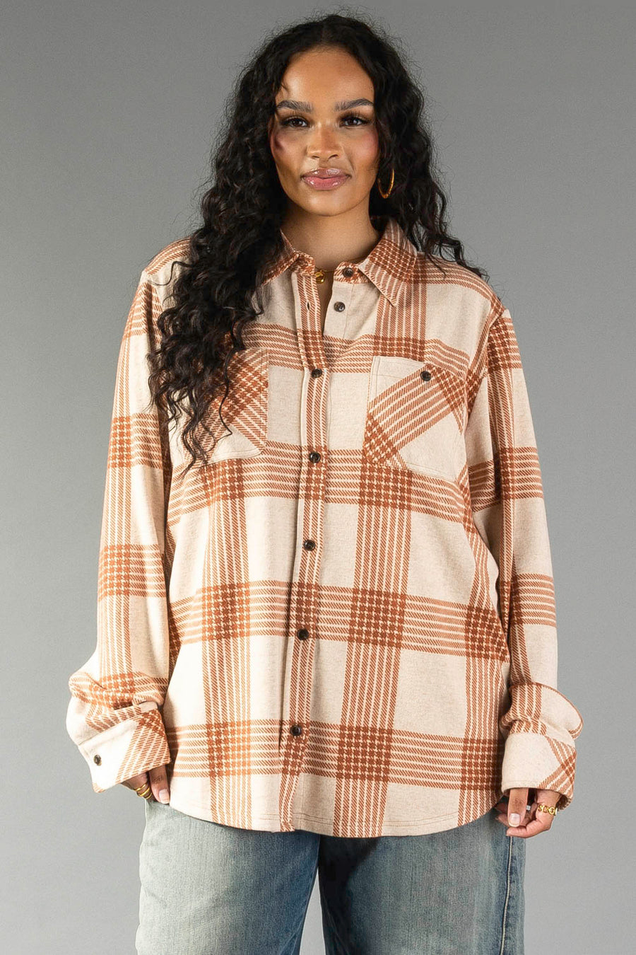 A woman with long curly hair wears the Panache Apparel Collection Cream & Rust Plaid Button Up paired with light blue jeans, standing against a plain gray background.