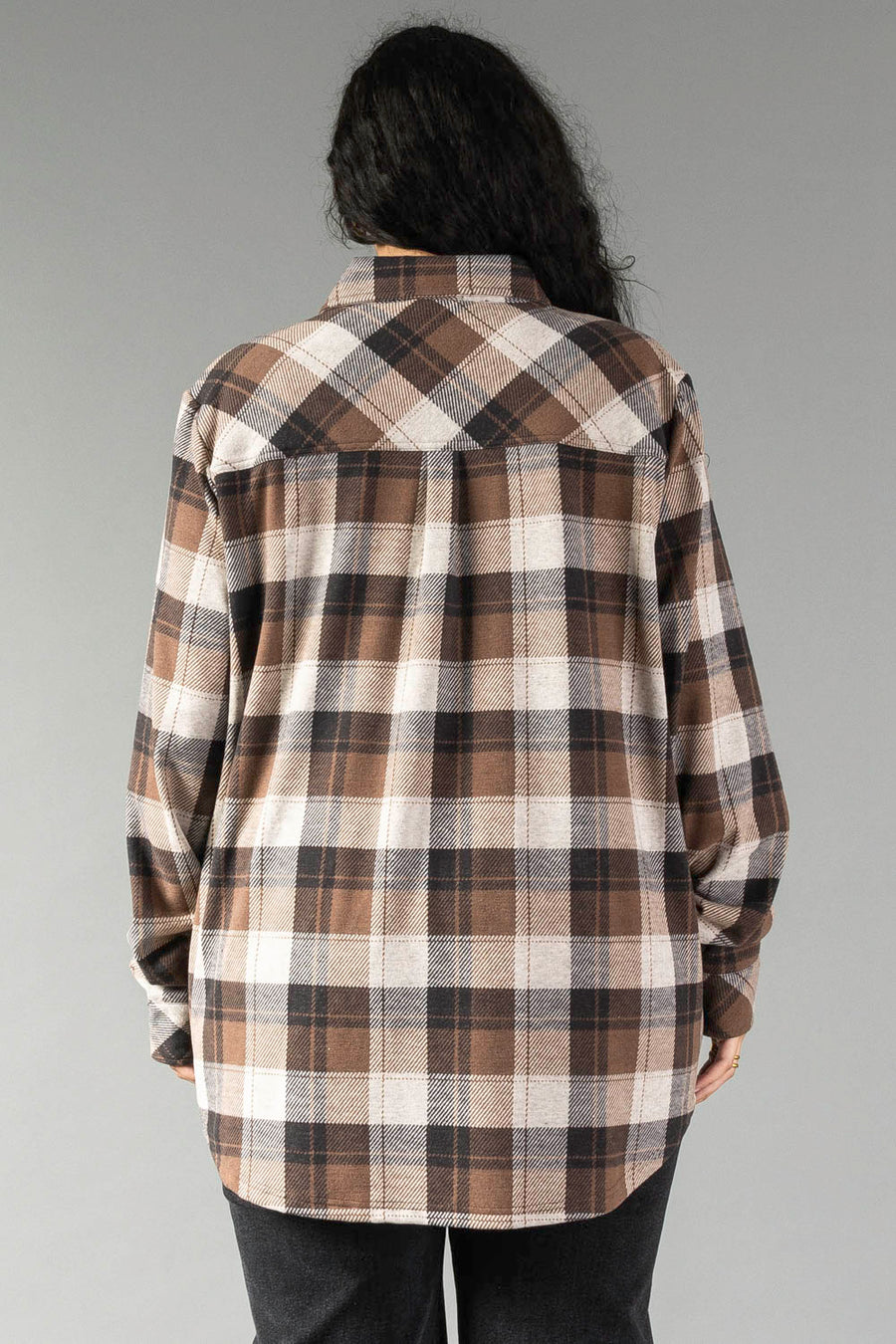 A person with long dark hair is standing facing away, wearing the Panache Apparel Collection Brown, Black & Cream Plaid Button Up with black pants against a plain gray background.