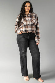A woman with long curly hair is wearing the Panache Apparel Collection Brown, Black & Cream Plaid Button Up shirt paired with black jeans. She stands facing forward, smiling, with one hand in her pocket and bare feet against a plain gray background.