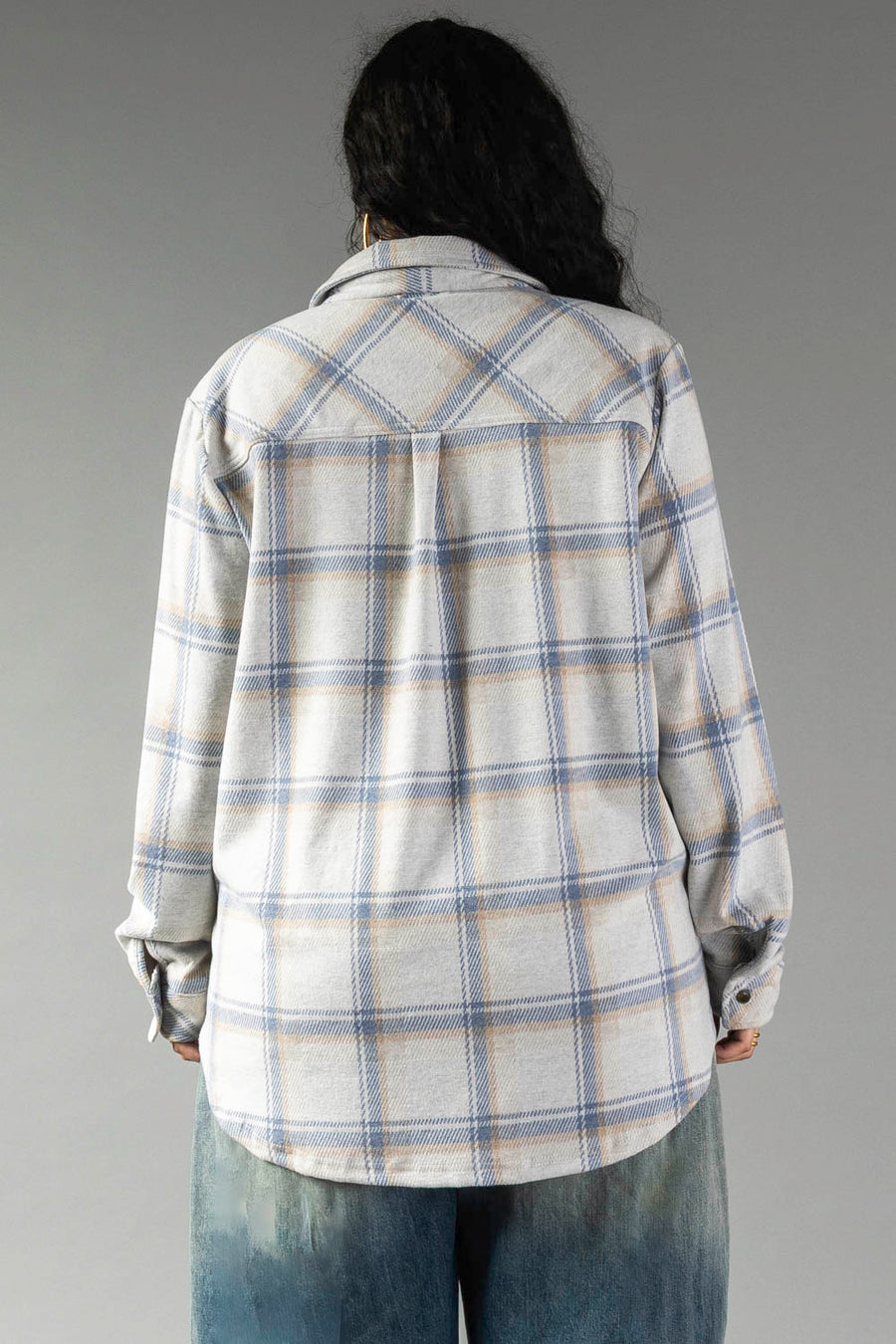 Person with long dark hair wearing the Panache Apparel Collection’s Cream, Dusty Blue & Tan Plaid Button Up and blue jeans, standing with their back to the camera against a plain gray background.