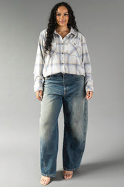 A woman with long dark hair stands against a plain gray background wearing the Panache Apparel Collection’s Cream, Dusty Blue & Tan Plaid Button Up paired with loose-fitting blue jeans. She has a relaxed expression and maintains a neutral stance.