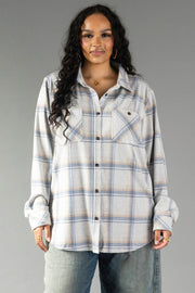 A woman with long curly hair wears the Panache Apparel Collection Cream, Dusty Blue & Tan Plaid Button Up, featuring front pockets, standing against a plain gray background.