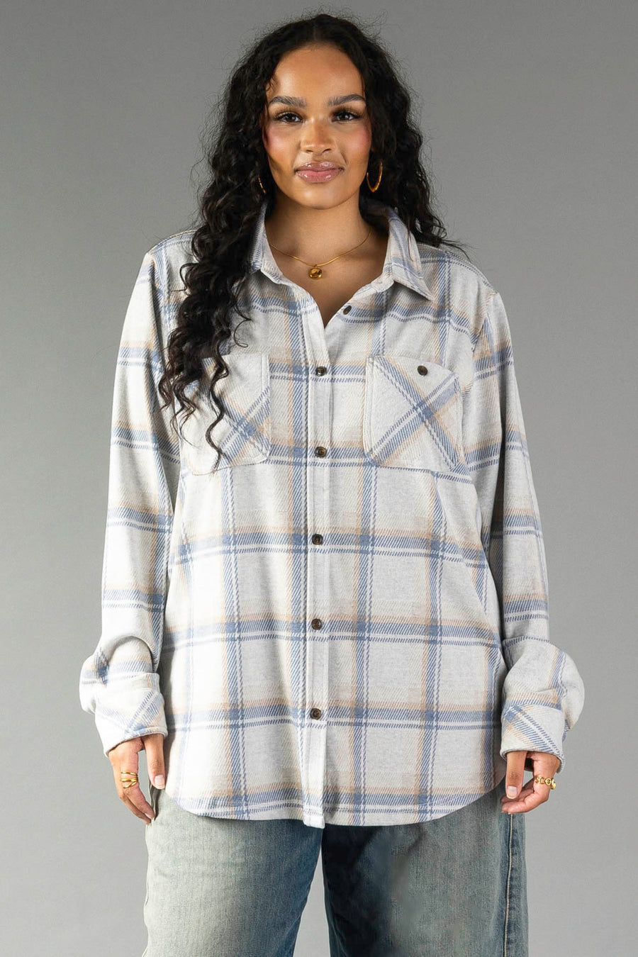 A woman with long curly hair wears the Panache Apparel Collection Cream, Dusty Blue & Tan Plaid Button Up, featuring front pockets, standing against a plain gray background.