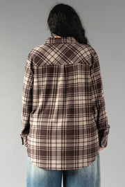 A person with long dark hair is seen from the back against a plain gray background, wearing the Panache Apparel Collection’s Chocolate Brown & Tan Plaid Button Up paired with blue jeans.