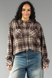 Wearing the Panache Apparel Collection’s Chocolate Brown & Tan Plaid Button Up with blue jeans, a woman with long curly hair stands against a plain gray background, smiling at the camera.