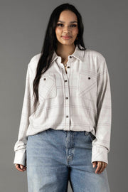 A woman with long dark hair wears the Panache Apparel Collection White & Light Gray Plaid Button Up and light blue jeans, standing and smiling against a plain gray background.