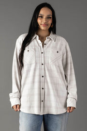 A woman with long dark hair wears the Panache Apparel Collection White & Light Gray Plaid Button Up, featuring front pockets, paired with light blue jeans as she stands against a plain gray background.