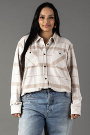 A woman with long dark hair wears the Panache Apparel Collection Cream, Tan & Gray Plaid Button Up paired with light blue jeans, standing against a plain gray background and smiling slightly.