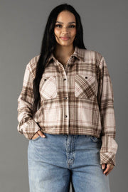 A woman with long dark hair models the Panache Apparel Collection’s Brown, Tan & Rose Plaid Button Up, paired with blue jeans. She stands against a plain gray background and smiles gently at the camera.