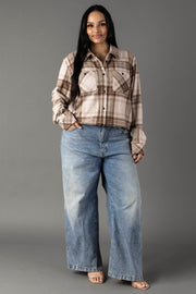 A woman stands against a gray background wearing the Brown, Tan & Rose Plaid Button Up from Panache Apparel Collection, paired with blue wide-leg jeans and sandals. She has long dark hair and is smiling slightly with one hand in her pocket.