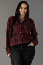 A woman with long dark hair smiles, wearing the Panache Apparel Collection Maroon & Black Plaid Button Up and black jeans, standing against a plain gray background.