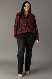 A woman with long dark hair stands smiling against a plain gray background, wearing the Panache Apparel Collection’s Maroon & Black Plaid Button Up shirt, black jeans, and open-toed shoes.