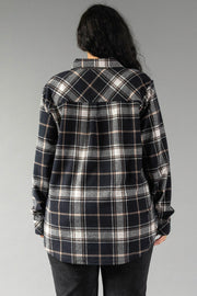 A person with long dark hair, seen from behind, wears the Panache Apparel Collection Black, White & Tan Plaid Button Up and dark pants, standing against a plain gray background.