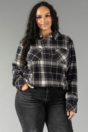A woman with long curly hair wears the Panache Apparel Collection Black, White & Tan Plaid Button Up paired with black jeans, standing with one hand in her pocket and smiling slightly against a plain gray background.