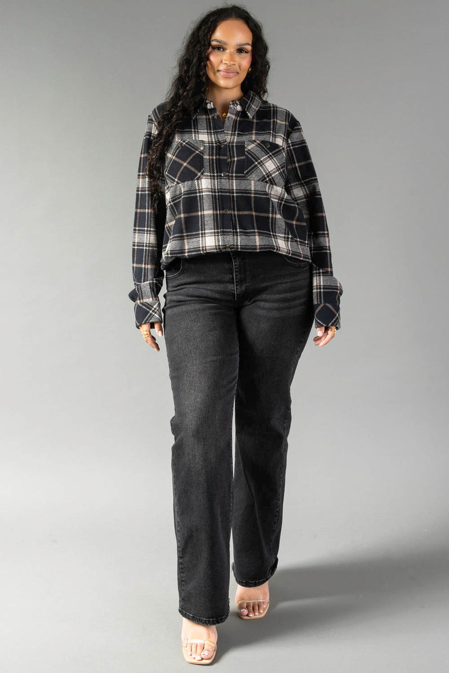 A woman models the Panache Apparel Collection Black, White & Tan Plaid Button Up, paired with black jeans and nude heels, as she stands against a plain gray background facing forward with a slight smile.