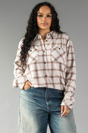A woman with long curly hair wears the Panache Apparel Collection Light Taupe & Brown Plaid Button Up and blue jeans, standing with one hand in her pocket against a gray background.