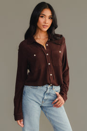 A woman with long dark hair wears the Panache Apparel Collection Espresso Brown Super Soft Button Up with chest pockets and light blue jeans, standing against a plain gray background.
