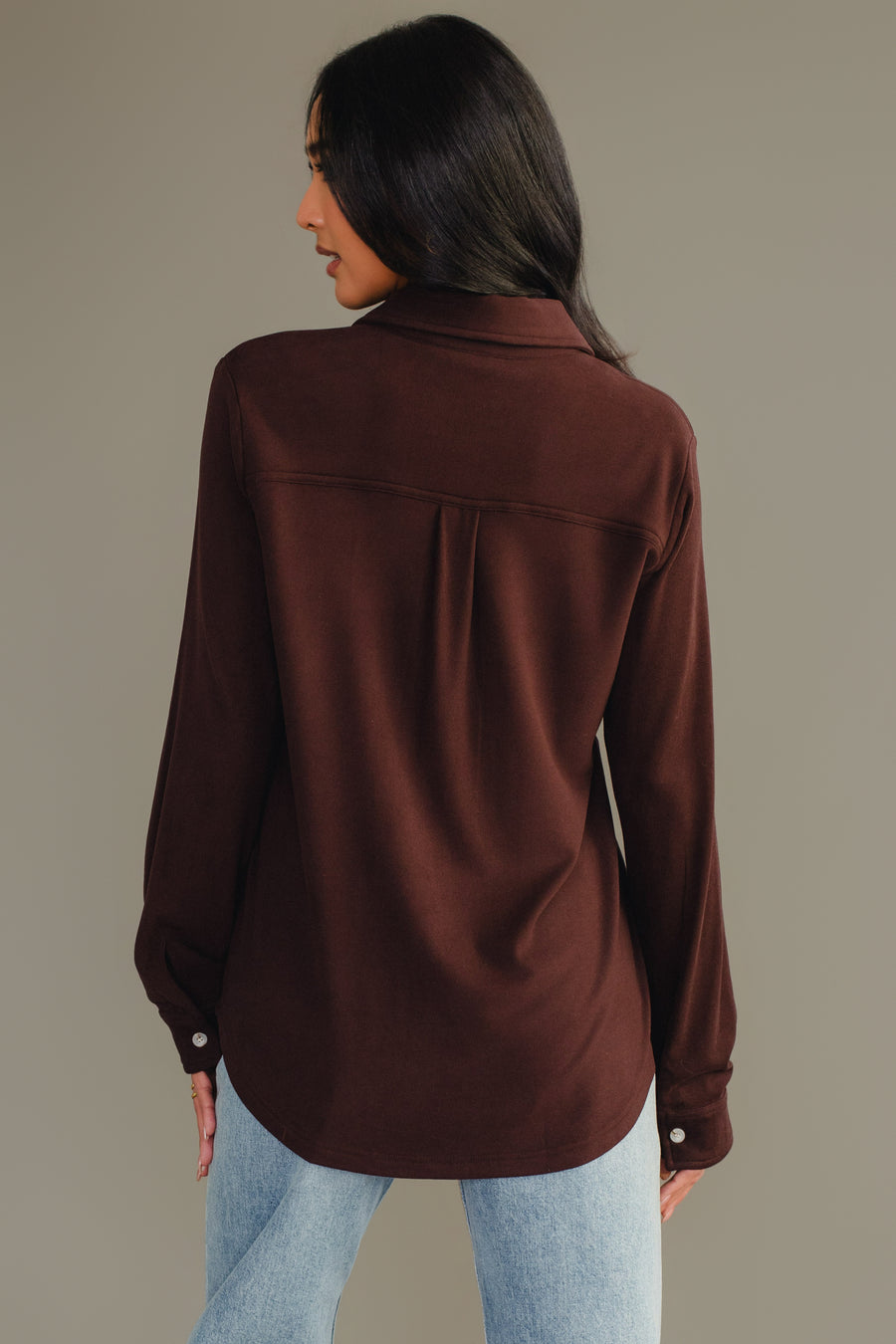 A woman with long dark hair, wearing the Panache Apparel Collection Espresso Brown Super Soft Button Up and light blue jeans, stands facing away from the camera against a plain background.