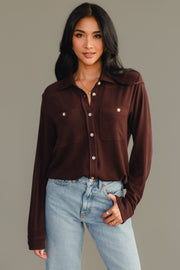A woman with long dark hair wears the Espresso Brown Super Soft Button Up from Panache Apparel Collection and light blue jeans, standing against a plain gray background and looking at the camera with a relaxed expression.