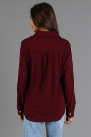 A person with long dark hair is shown from the back, wearing the Panache Apparel Collection Burgundy Soft Button Up and light blue jeans, standing against a plain gray background.