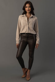 A woman stands against a gray background, wearing the Light Tan Soft Button Up from Panache Apparel Collection, paired with black leather pants and tan pointed-toe heels. She has long dark hair and a relaxed, confident pose with one leg slightly bent.