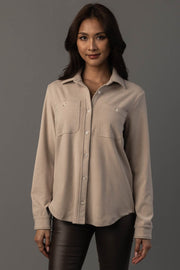 A woman with long dark hair is wearing the Panache Apparel Collection Light Tan Soft Button Up with front pockets and black pants, standing against a plain gray background, facing the camera and smiling slightly.