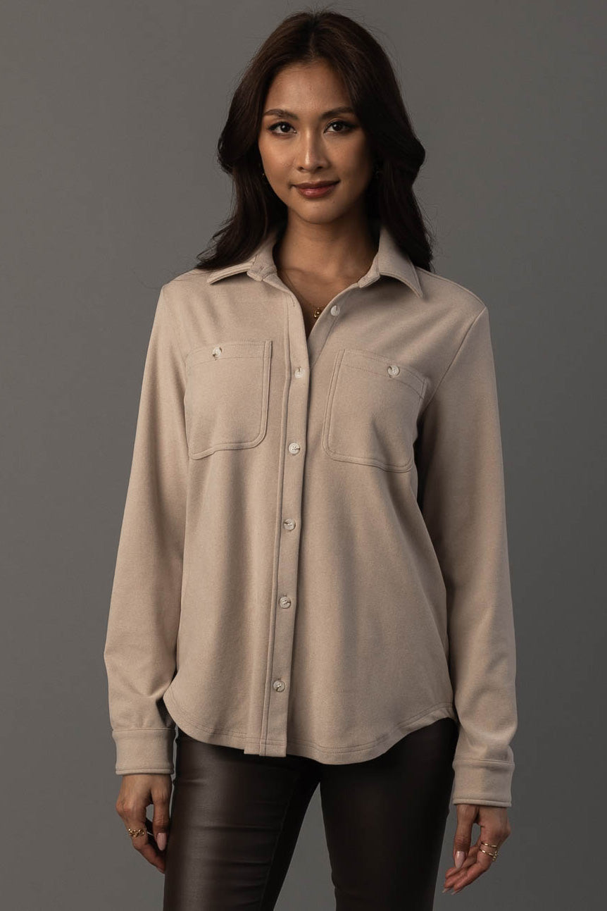 A woman with long dark hair is wearing the Panache Apparel Collection Light Tan Soft Button Up with front pockets and black pants, standing against a plain gray background, facing the camera and smiling slightly.