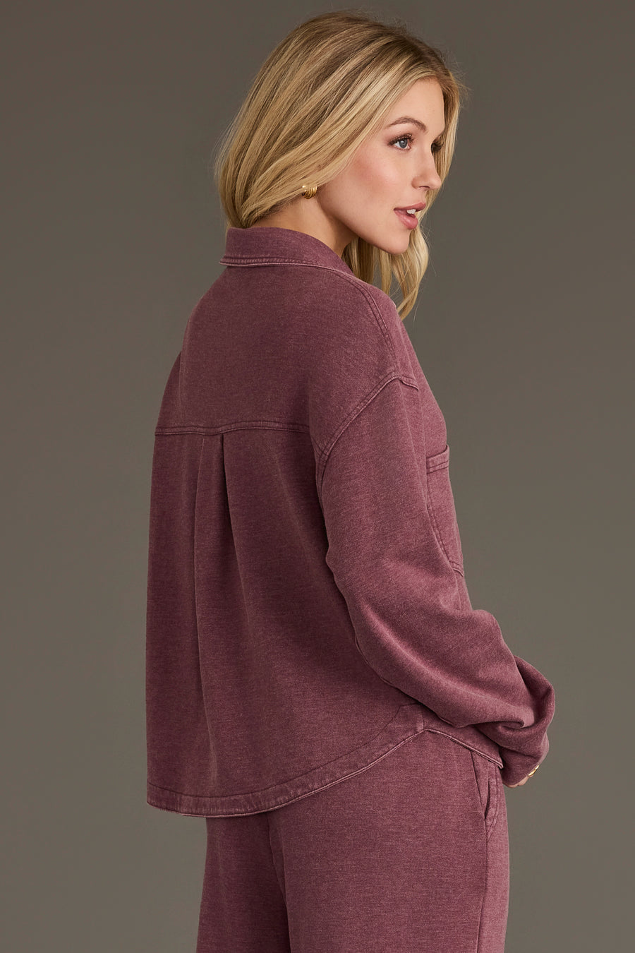 A woman with long blonde hair is shown standing sideways and looking to the right against a plain background, wearing the Panache Apparel Collection’s Merlot Cropped Washed Soft Button Up with matching pants.