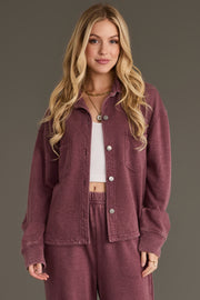 A woman with long blonde hair is wearing the Merlot Cropped Washed Soft Button Up and matching pants from Panache Apparel Collection over a white ribbed crop top, standing against a plain gray background.