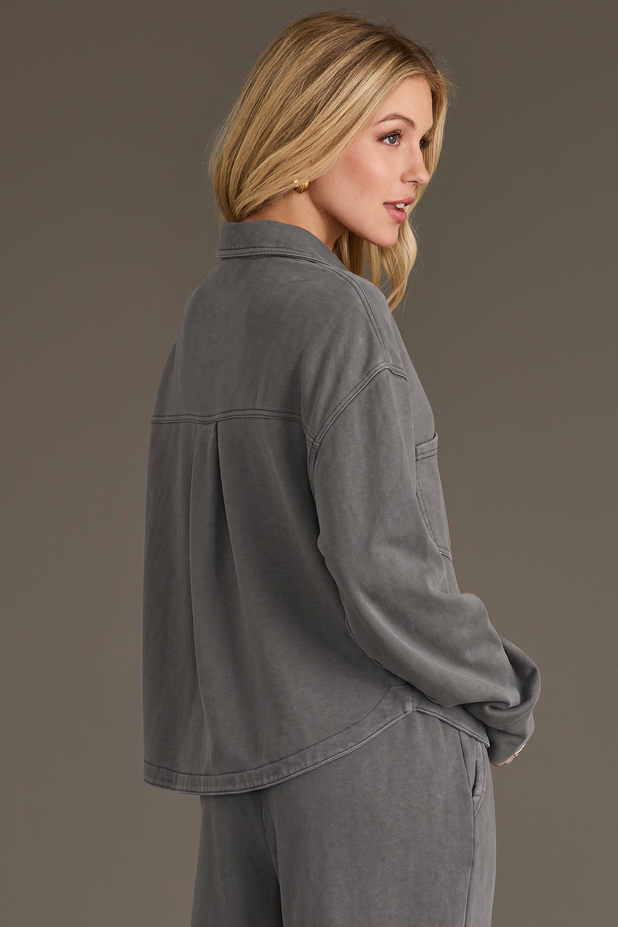 A woman with long blonde hair models the Panache Apparel Collection Gray Cropped Washed Soft Button Up, paired with matching pants, as she stands sideways against a plain background.