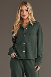 A woman wears a Pine Green Cropped Washed Soft Button Up, a pine green cropped button-up shirt in a soft washed fabric featuring long sleeves and two chest pockets.