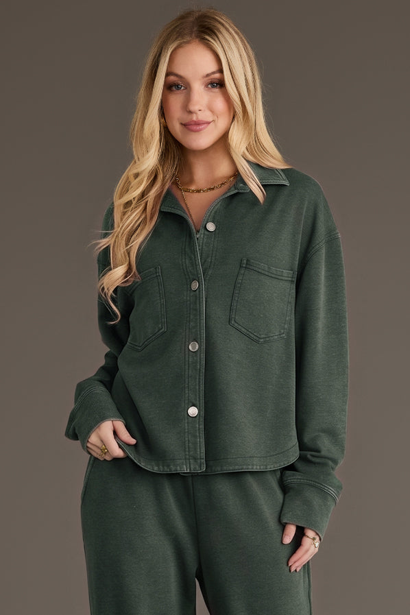 A woman wears a Pine Green Cropped Washed Soft Button Up, a pine green cropped button-up shirt in a soft washed fabric featuring long sleeves and two chest pockets.