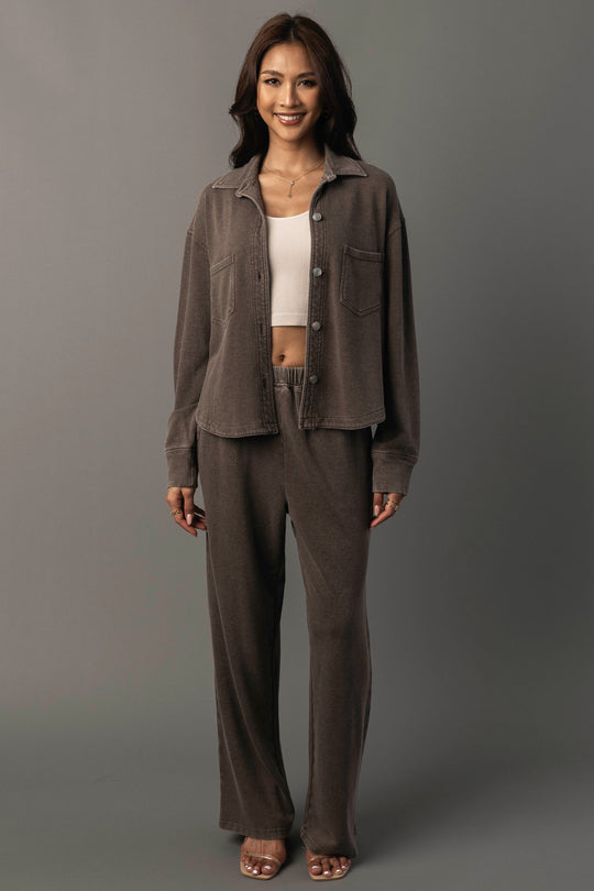 A woman stands smiling against a plain gray background, wearing the Panache Apparel Collection’s Cocoa Cropped Washed Soft Button Up with matching brown pants, a white cropped top, and open-toed heels.