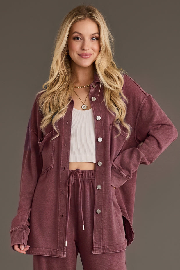 A woman wears an unbuttoned, Merlot washed Merlot Washed Soft Button Up by Panache Apparel Collection over a white crop top and matching burgundy sweatpants.