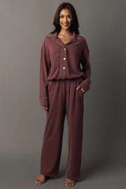 A woman stands smiling with her left hand in her pocket, wearing the Panache Apparel Collection Merlot Washed Soft Button Up and matching wide-leg pants against a plain grey background.