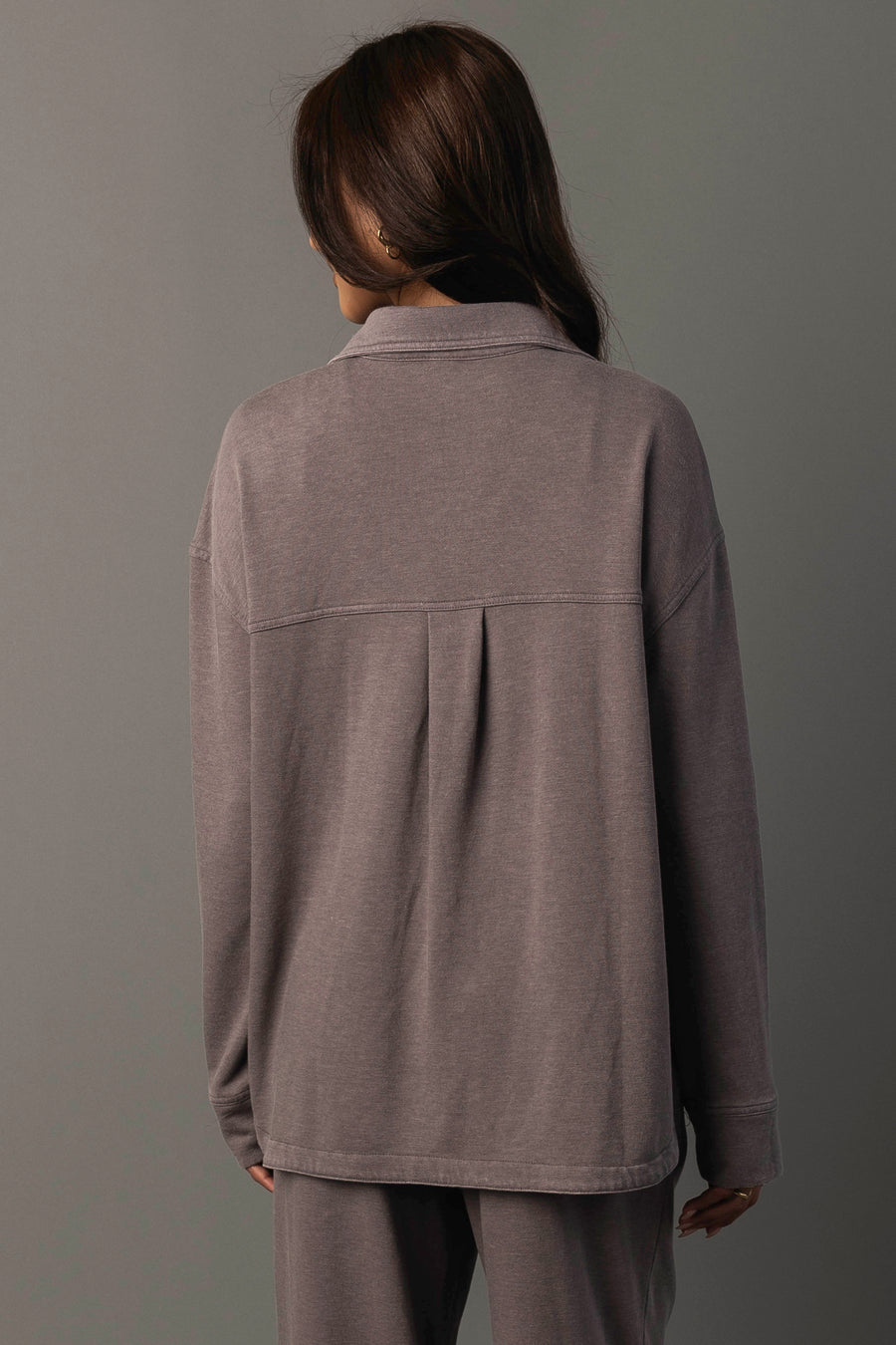 A person with long brown hair stands facing away against a plain gray background, wearing the Panache Apparel Collection Gray Washed Soft Button Up with matching pants.