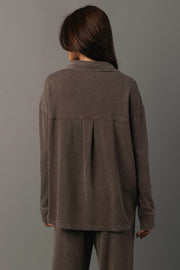 A person with long brown hair stands facing away, wearing the Panache Apparel Collection Cocoa Washed Soft Button Up and matching pants against a neutral gray background.
