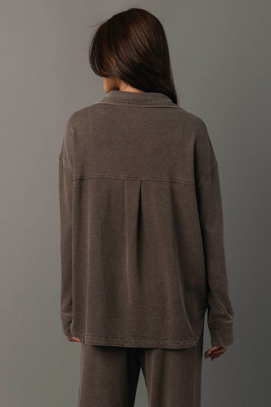 A person with long brown hair stands facing away, wearing the Panache Apparel Collection Cocoa Washed Soft Button Up and matching pants against a neutral gray background.