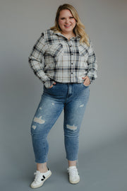 A smiling woman with long blonde hair wears the Panache Apparel Collection Black, Light Gray & Brown Plaid Button Up, paired with blue ripped jeans and white sneakers, standing with her hands in her pockets against a gray backdrop.
