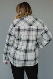 A person with wavy blonde hair, wearing the Panache Apparel Collection Black, Light Gray & Brown Plaid Button Up long sleeve shirt and black pants, stands facing away from the camera against a plain gray background.